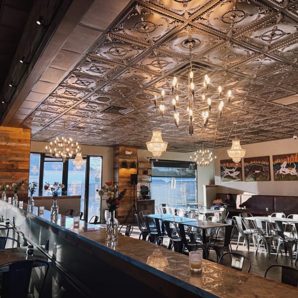 Restaurant interior with ornate ceiling, chandeliers, wooden accents, and tables set for dining.