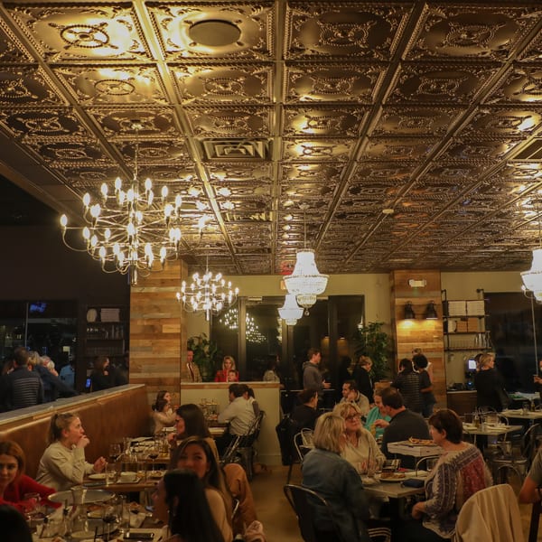 A bustling restaurant interior with patrons dining under ornate gold ceilings and chandeliers.