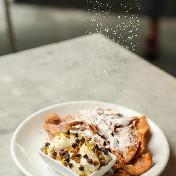 Powdered sugar being sifted over a plate of dessert with cannoli chips and ricotta cream.