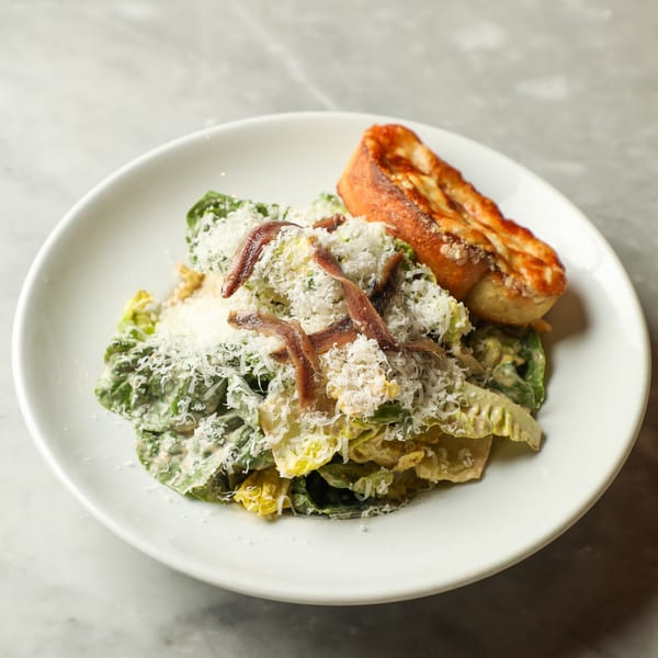 Caesar salad with anchovies, shredded cheese, and a side of toasted bread on a white plate.